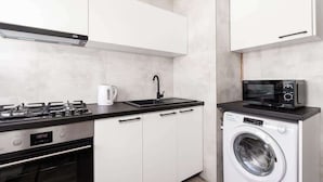 A compact kitchen with a gas stove, a sink, a microwave, and a washing machine. - Elegant Apartment in Wroclaw | Close to Main Railway Station (Wroclaw)