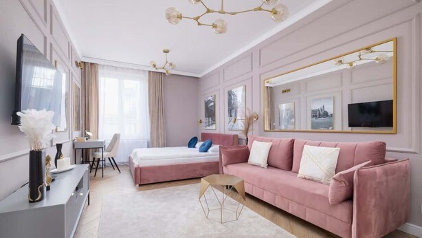 A modern bedroom with a pink sofa, a bed, a desk, and a large mirror. - Elegant Apartment | Air Conditioning, Balcony, Close to Market Square (Kraków)