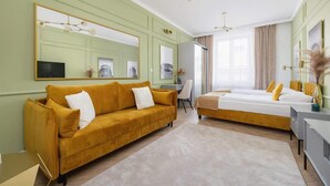 A hotel room with a mustard-colored sofa, a bed with yellow pillows, a desk, and a large mirror. - Elegant Apartment | Air Conditioning, Balcony, Close to Market Square (Kraków)