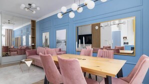 A modern dining area with a wooden table and pink upholstered chairs, large mirrors, and a blue wall. - Elegant Apartment | Air Conditioning, Balcony, Close to Market Square (Kraków)