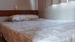 A bedroom with a bed, a wooden headboard, a wall socket, and a window with curtains. - Bungalow con Encanto a 600 Metros de la Playa las 3 Piedras. Aceptamos Mascotas (Chipiona)