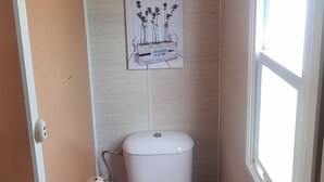 A small, compact bathroom with a toilet, a small trash bin, a toilet paper holder, and a shelf above the toilet. - Bungalow con Encanto a 600 Metros de la Playa las 3 Piedras. Aceptamos Mascotas (Chipiona)