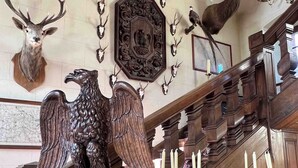 A grand staircase with ornate woodwork, a mounted eagle sculpture, and various animal head mounts on the walls. - Château de La Rivière (Pontgouin)