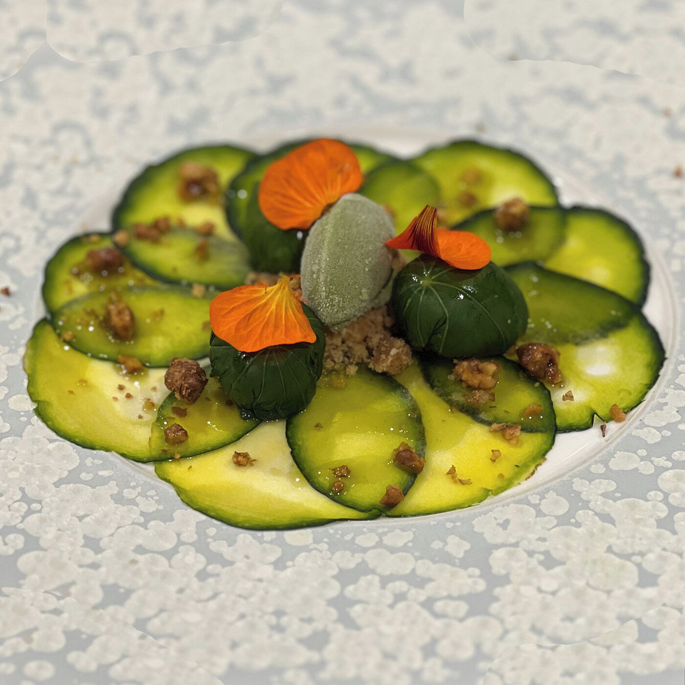 Une assiette de rondelles de concombre disposées en cercle, agrémentée de noix et d’un élément décoratif au centre.
