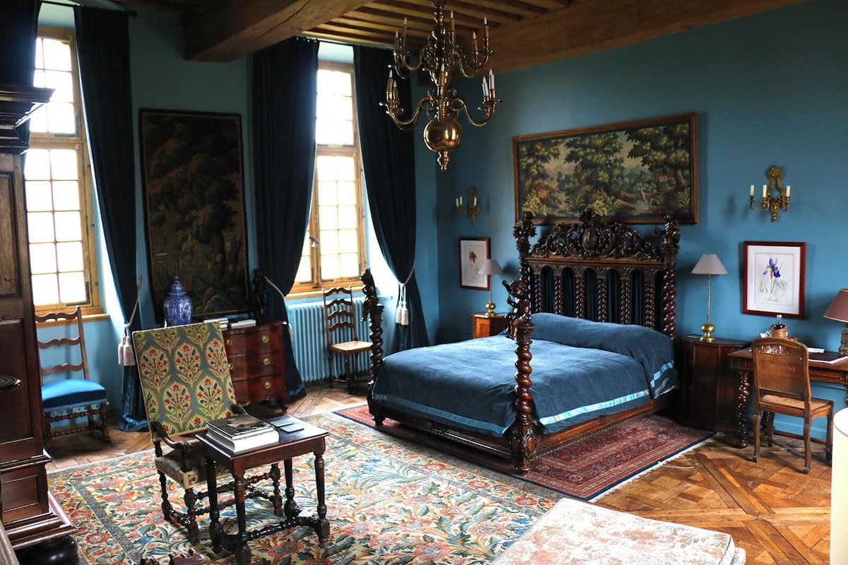 A traditional bedroom with a four-poster bed, a chandelier, and a large painting on the wall.