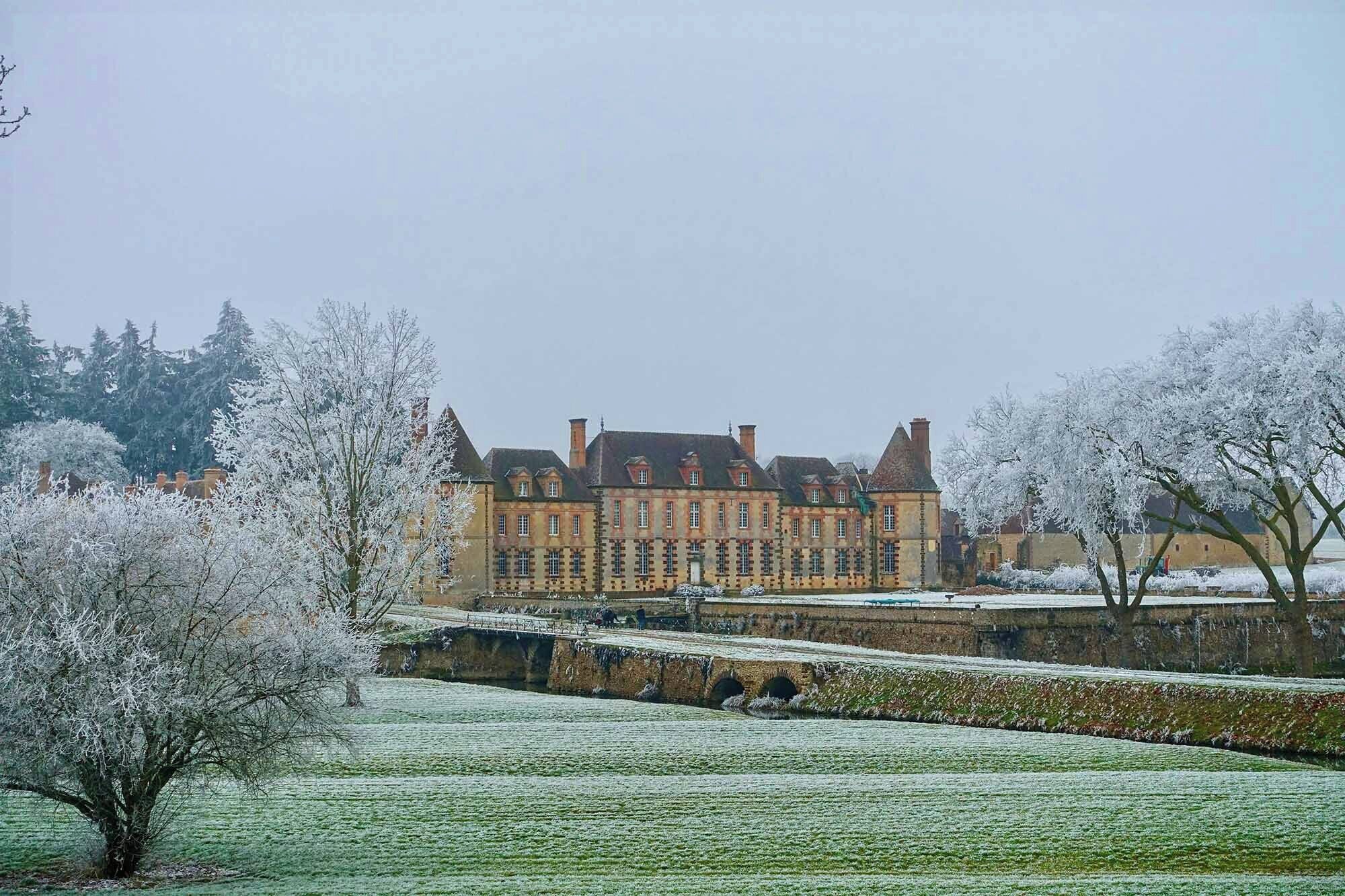 A large, historic building with multiple windows and a symmetrical facade, surrounded by snow-covered trees and a manicured lawn.