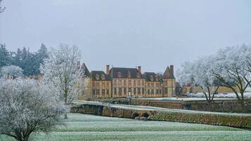 A large, historic building with multiple windows and a symmetrical facade, surrounded by snow-covered trees and a manicured lawn.