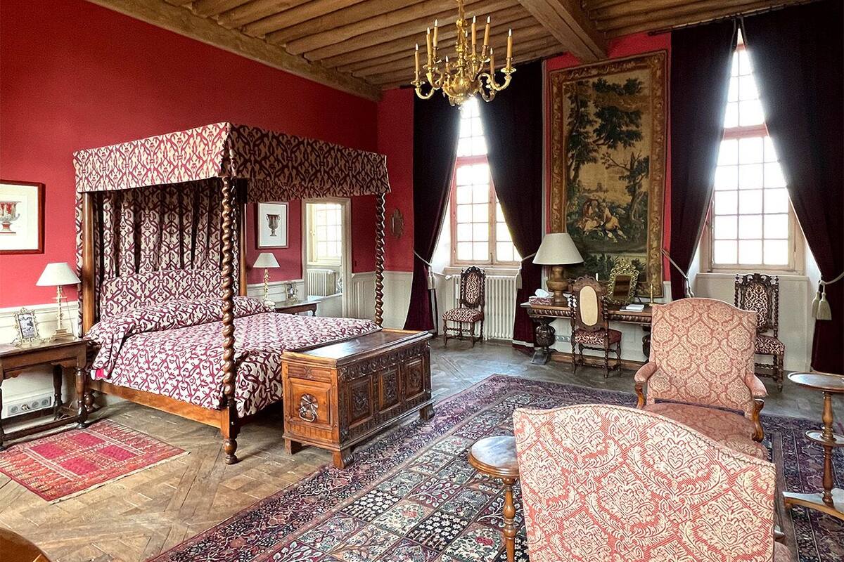 A traditional bedroom with a four-poster bed, a wooden chest, and a red carpet.