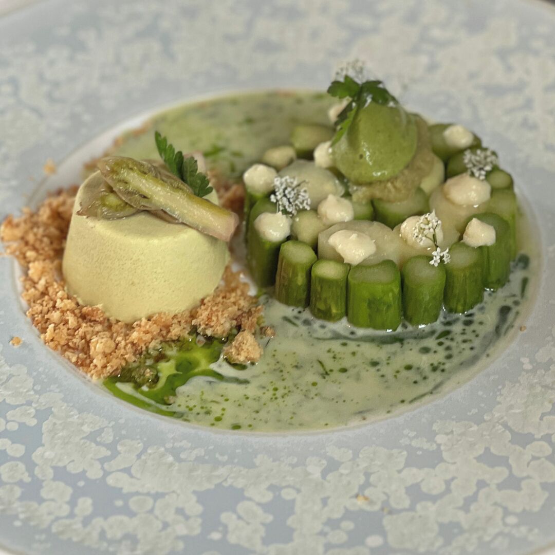 A dessert with a spherical component, green cylindrical pieces, and a crumbly base on a plate.
