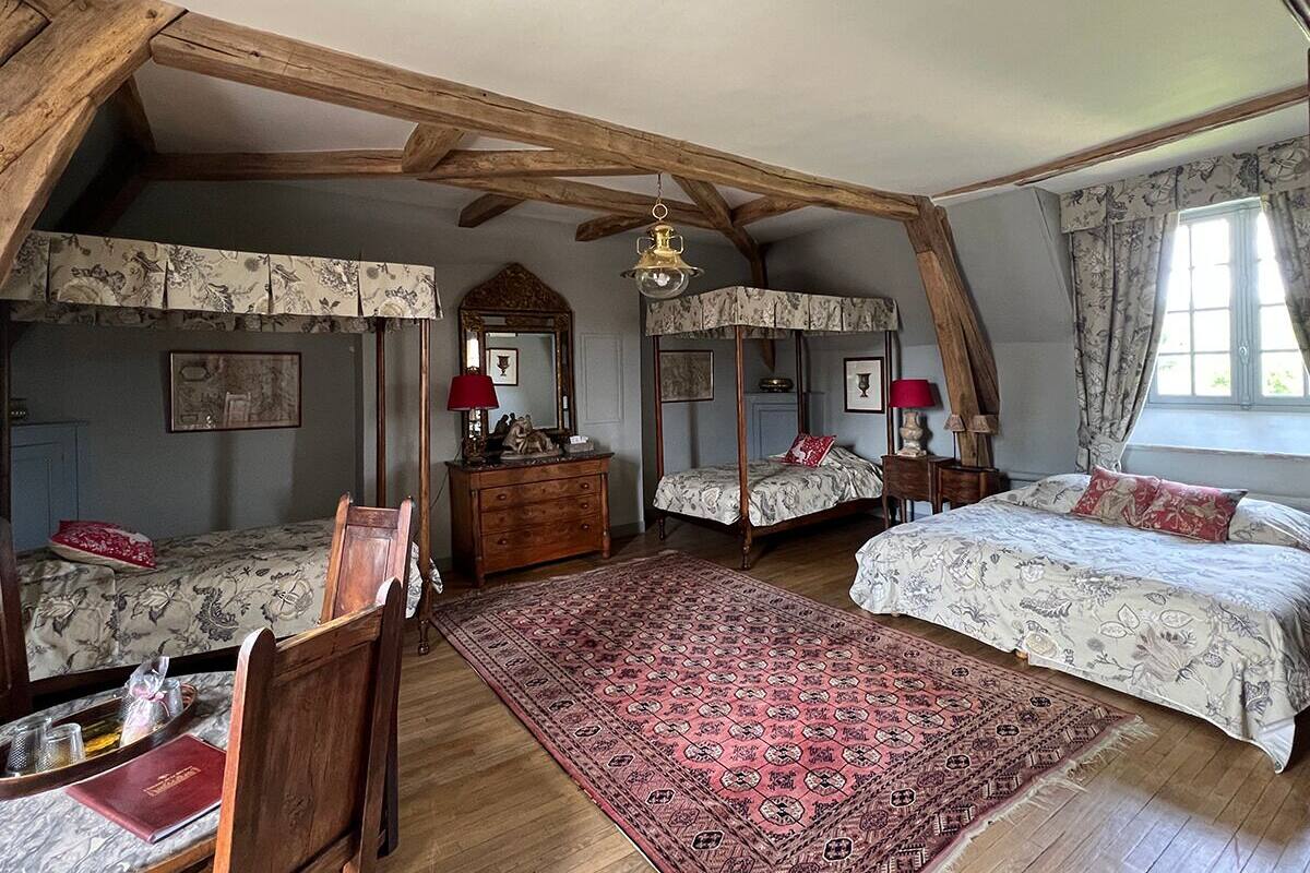 A bedroom with two single beds, a wooden dresser, a red rug, and a large window with curtains.