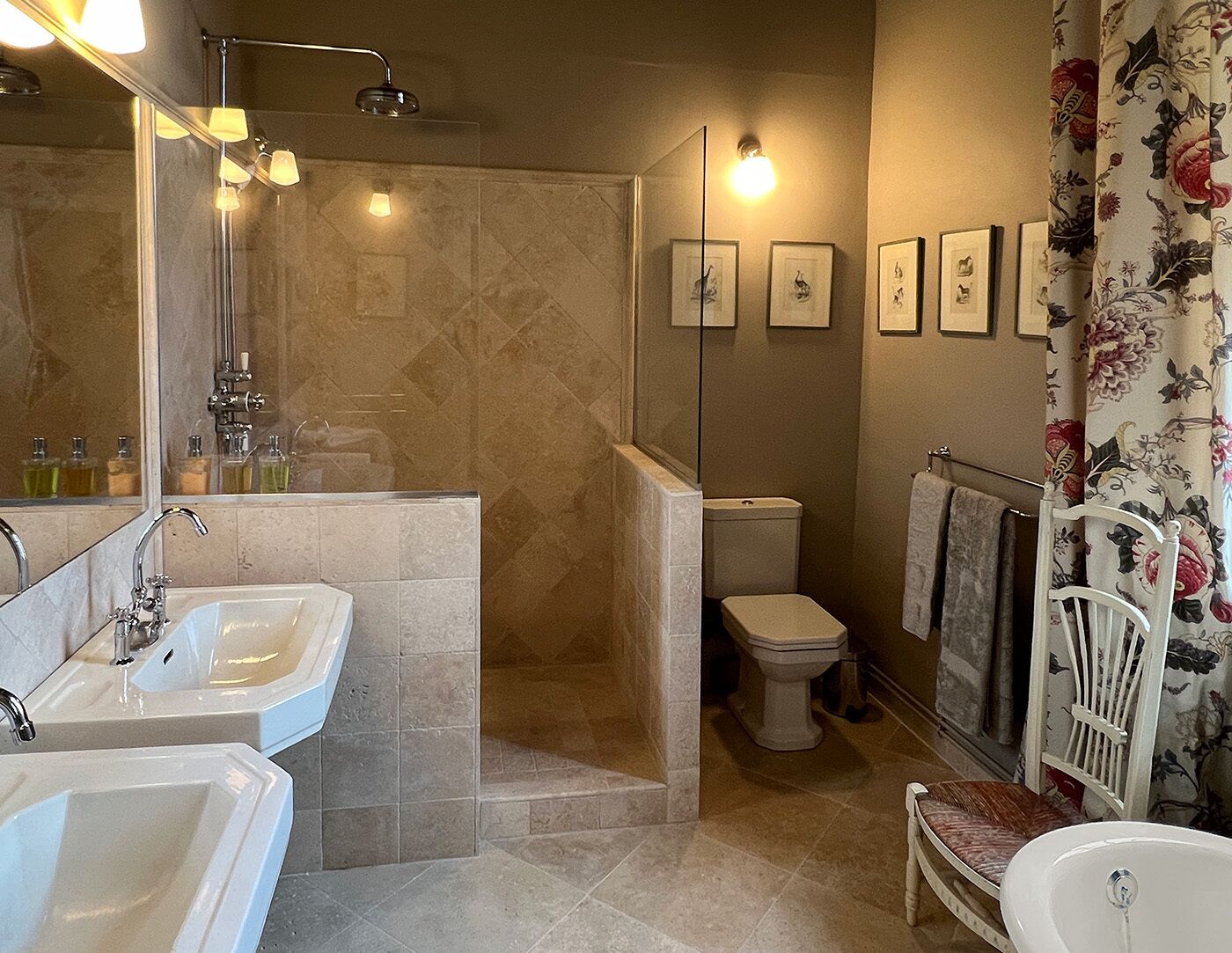 A bathroom with a shower, two sinks, a toilet, and framed pictures on the wall.