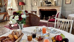 A dining area with a table set for breakfast, including bread, pastries, fruit, and beverages. - Château de La Rivière (Pontgouin)