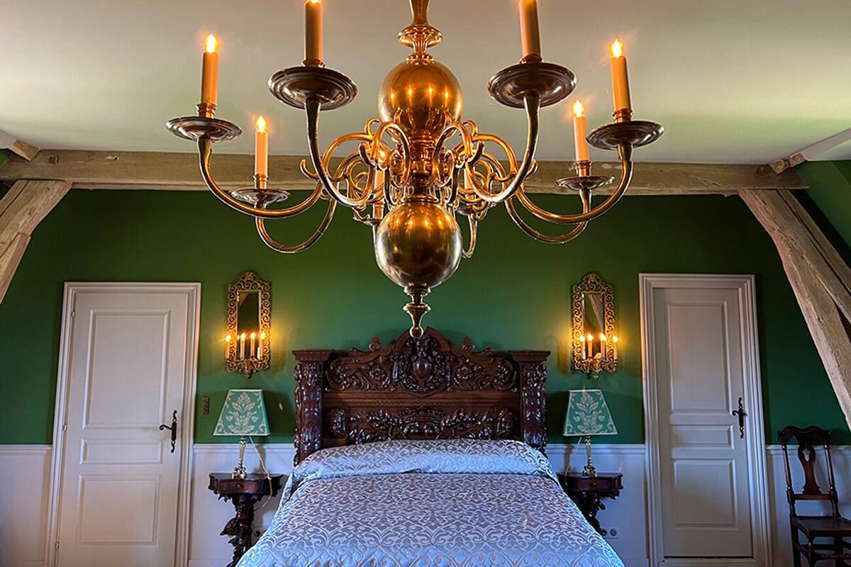 A bedroom with a large ornate chandelier, a wooden bed with a patterned bedspread, and two wall-mounted lamps.