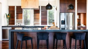 A modern kitchen with a central island, bar stools, a stainless steel refrigerator, and wooden cabinetry.