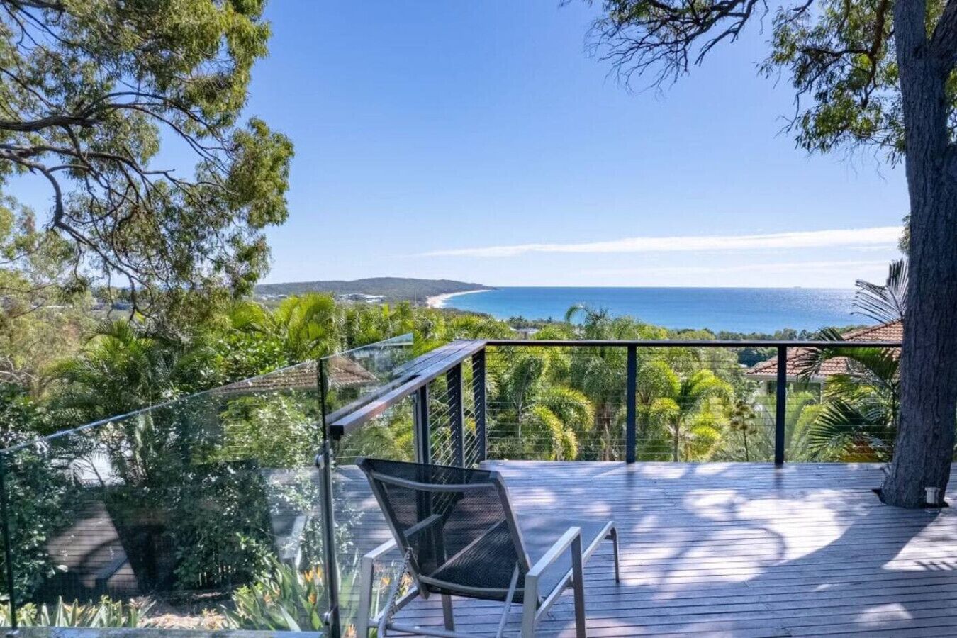 A deck with a chair, overlooking a coastal landscape with trees and a view of the sea.
