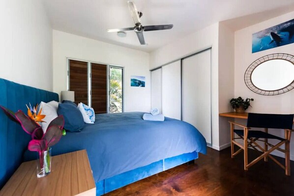 A bedroom with a bed, a desk, a chair, a ceiling fan, and a window.