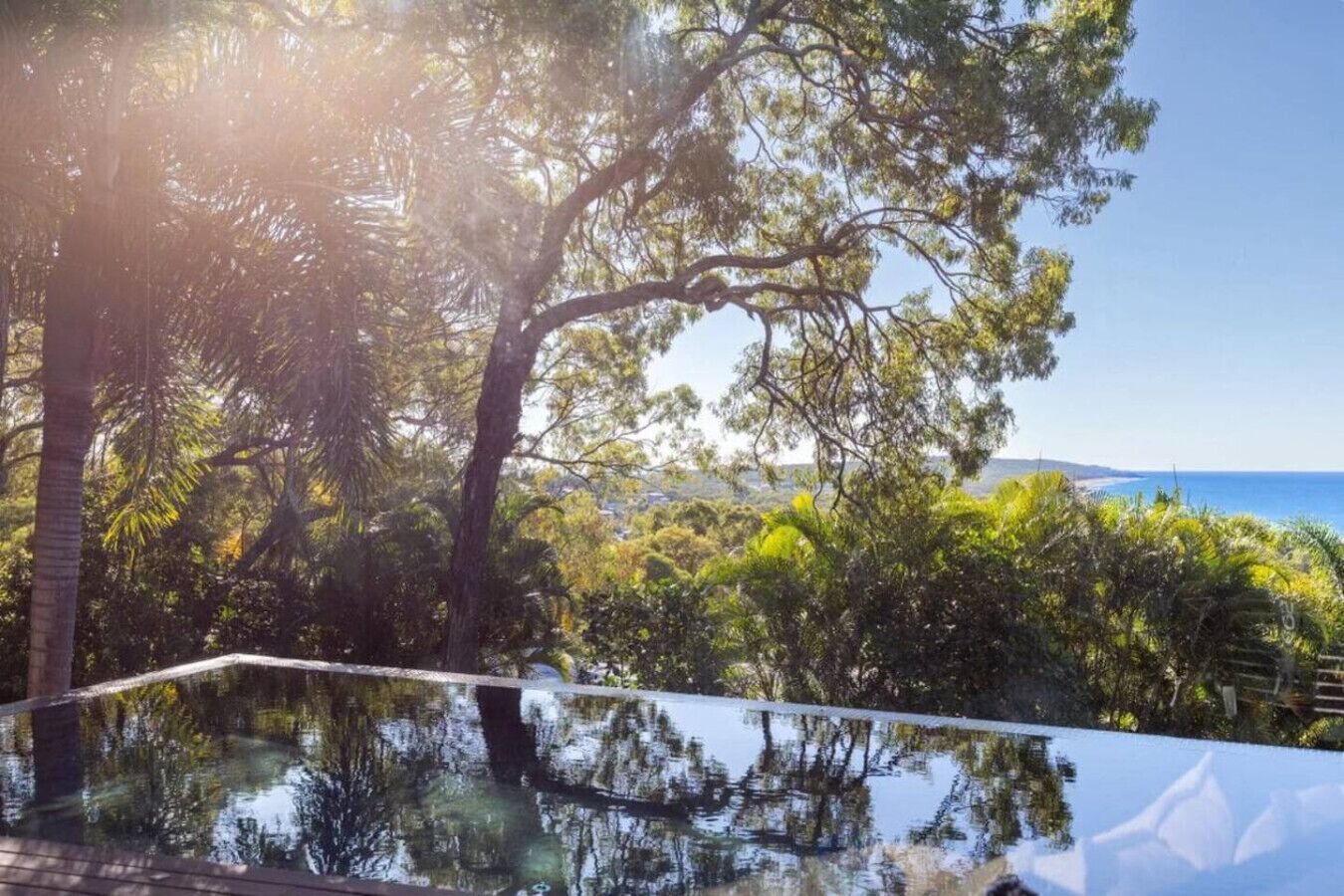 A pool with a clear view of the ocean and surrounding trees.