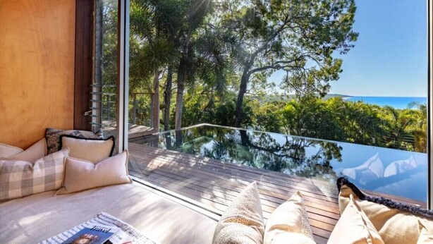 A balcony with a wooden floor, a glass railing, and a view of trees and the sea.