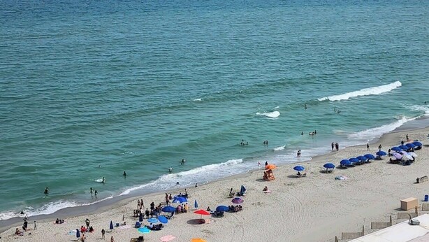 A beach with people, umbrellas, and a building. - Beach Life Oceanview Efficiency DW 1503 (Myrtle Beach)