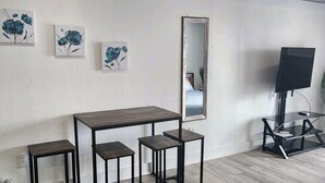 A room with a wooden table, two stools, a TV on a stand, and three floral paintings on the wall. - Beach Life Oceanview Efficiency DW 1503 (Myrtle Beach)