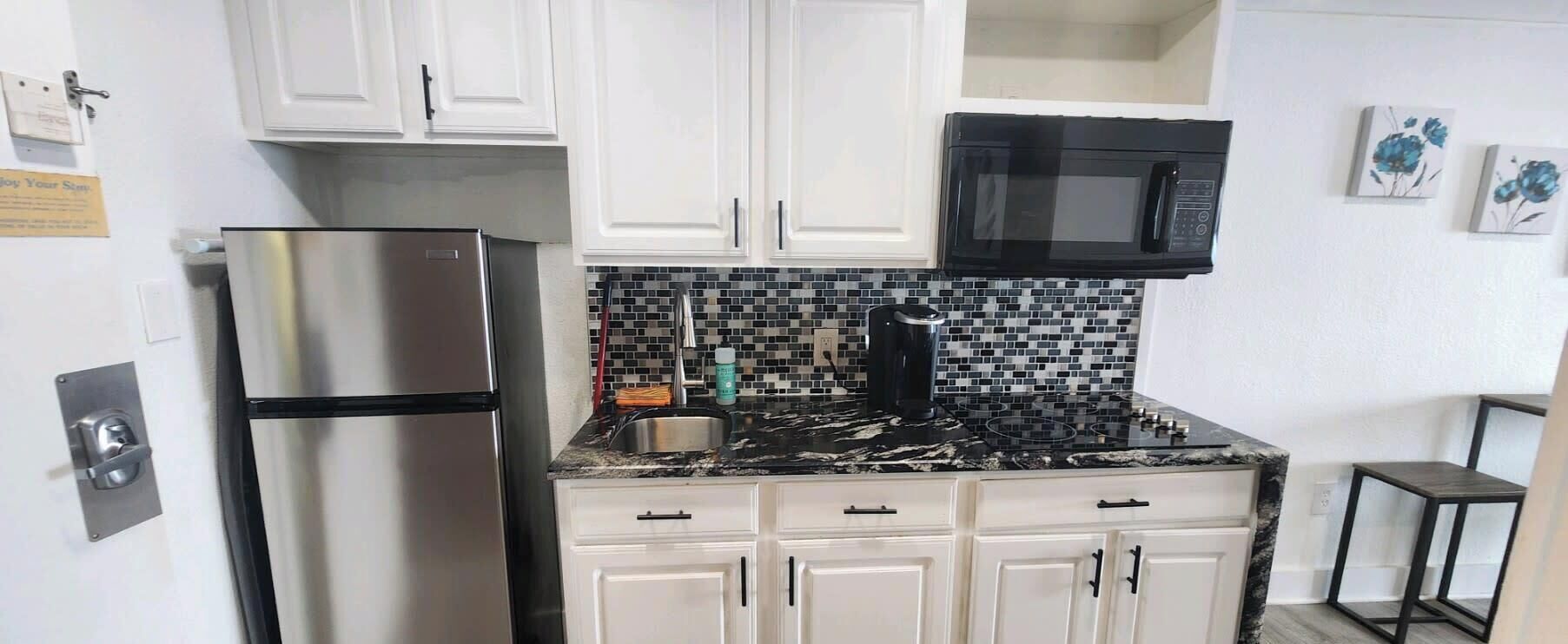 A kitchen with white cabinets, a stainless steel refrigerator, a black microwave, and a tiled backsplash.