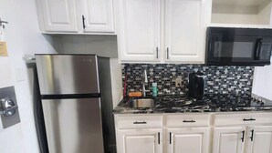 A kitchen with white cabinets, a stainless steel refrigerator, a black microwave, and a tiled backsplash. - Beach Life Oceanview Efficiency DW 1503 (Myrtle Beach)