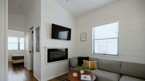 A living room with a grey sofa, a small round wooden coffee table, a fireplace, and a TV mounted on the wall.
