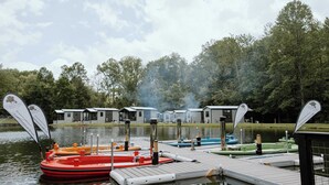 A lakeside dock with several boats, a wooden pier, and a row of cabins in the background.