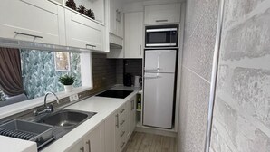A modern kitchen with white cabinetry, a double sink, a microwave, and a refrigerator.