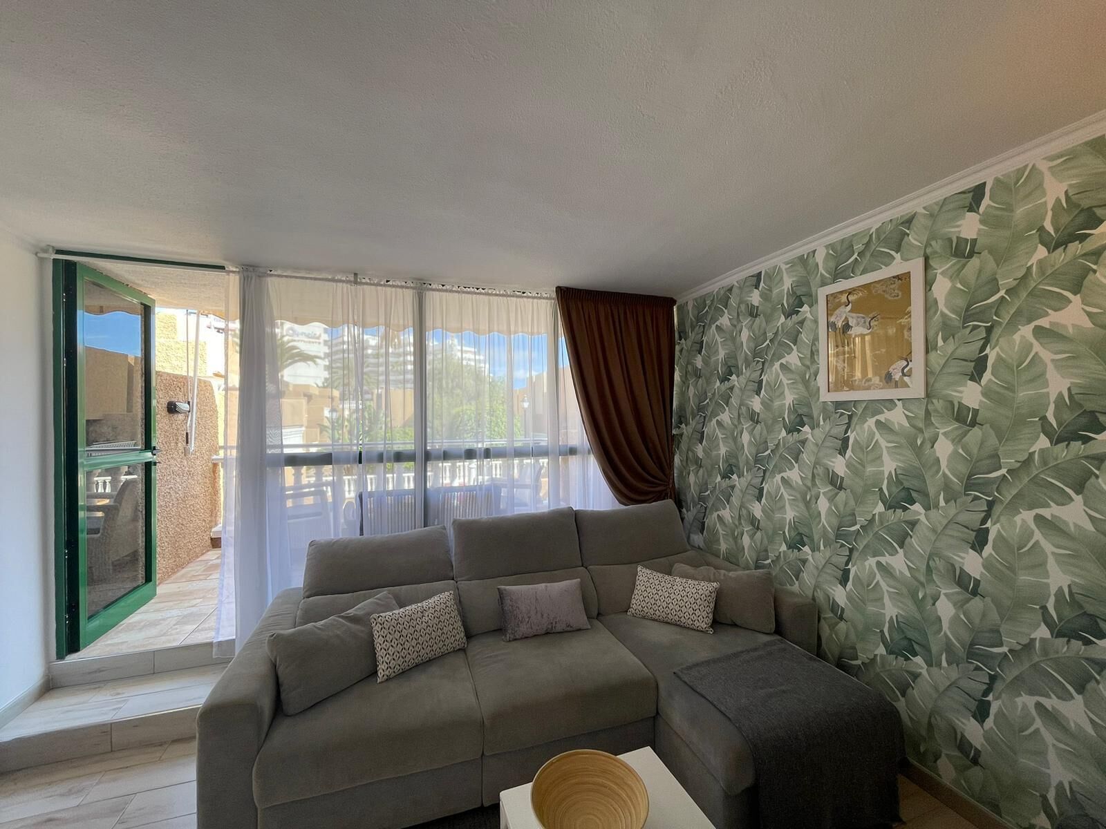 A living room with a grey sectional sofa, a white coffee table, and a large window with sheer curtains.
