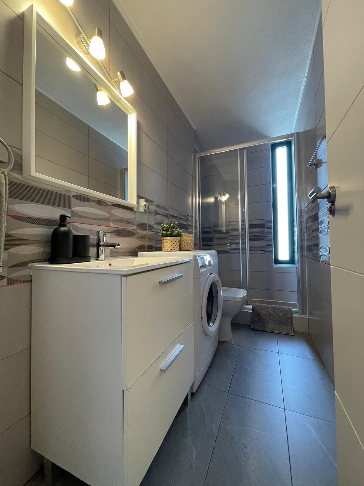A modern bathroom with a built-in washing machine, a toilet, and a shower area.