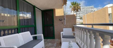 A balcony with white wicker furniture, including a sofa and a table with a lantern.