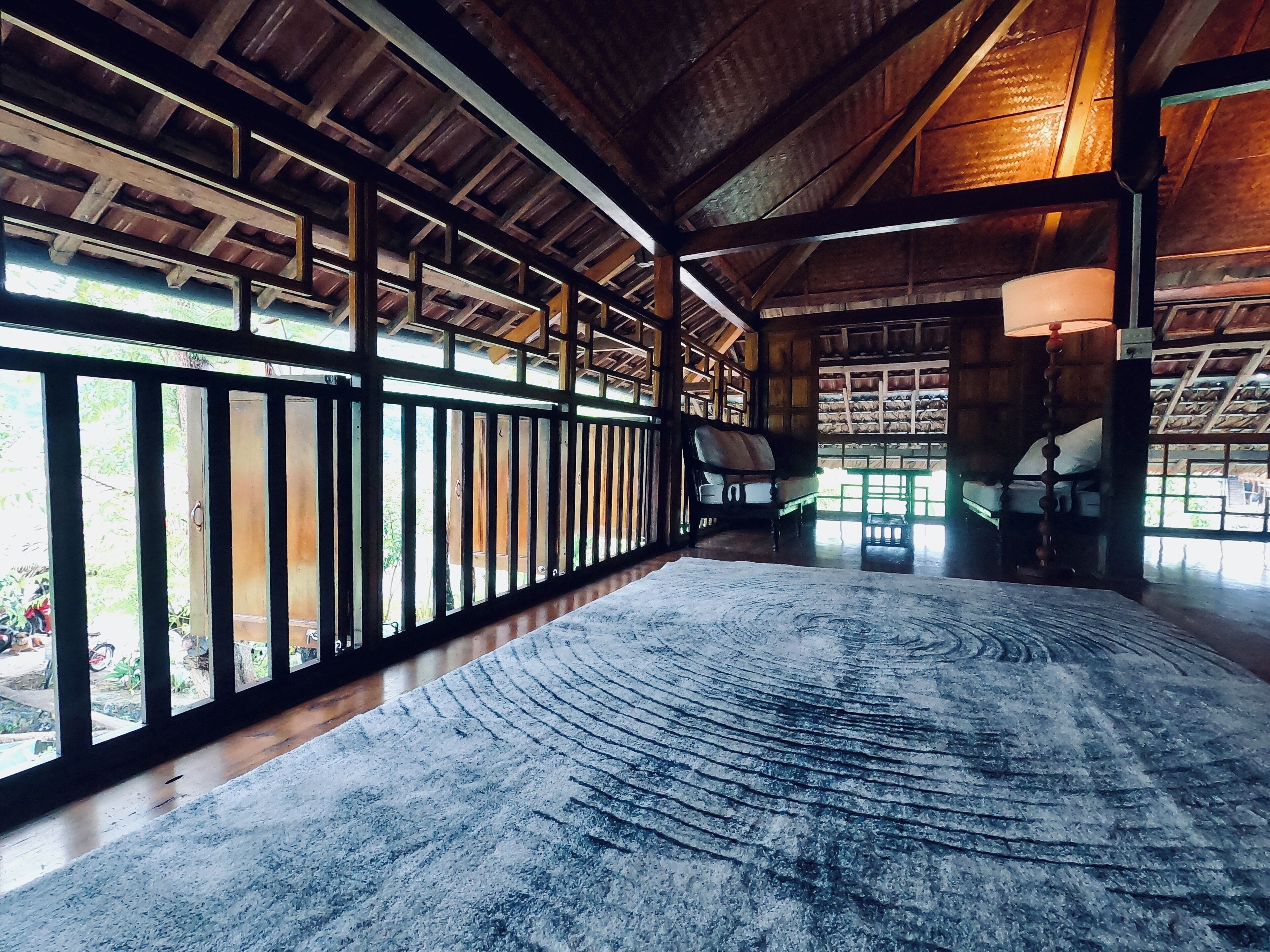 A spacious room with a high ceiling, wooden beams, a large window, and a patterned rug.