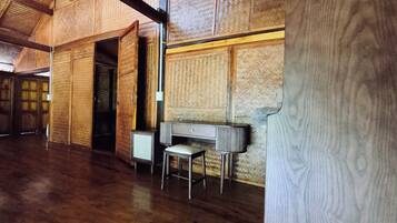 A spacious room with wooden floors, a large open doorway, a small table with a chair, and a wall with a woven pattern.