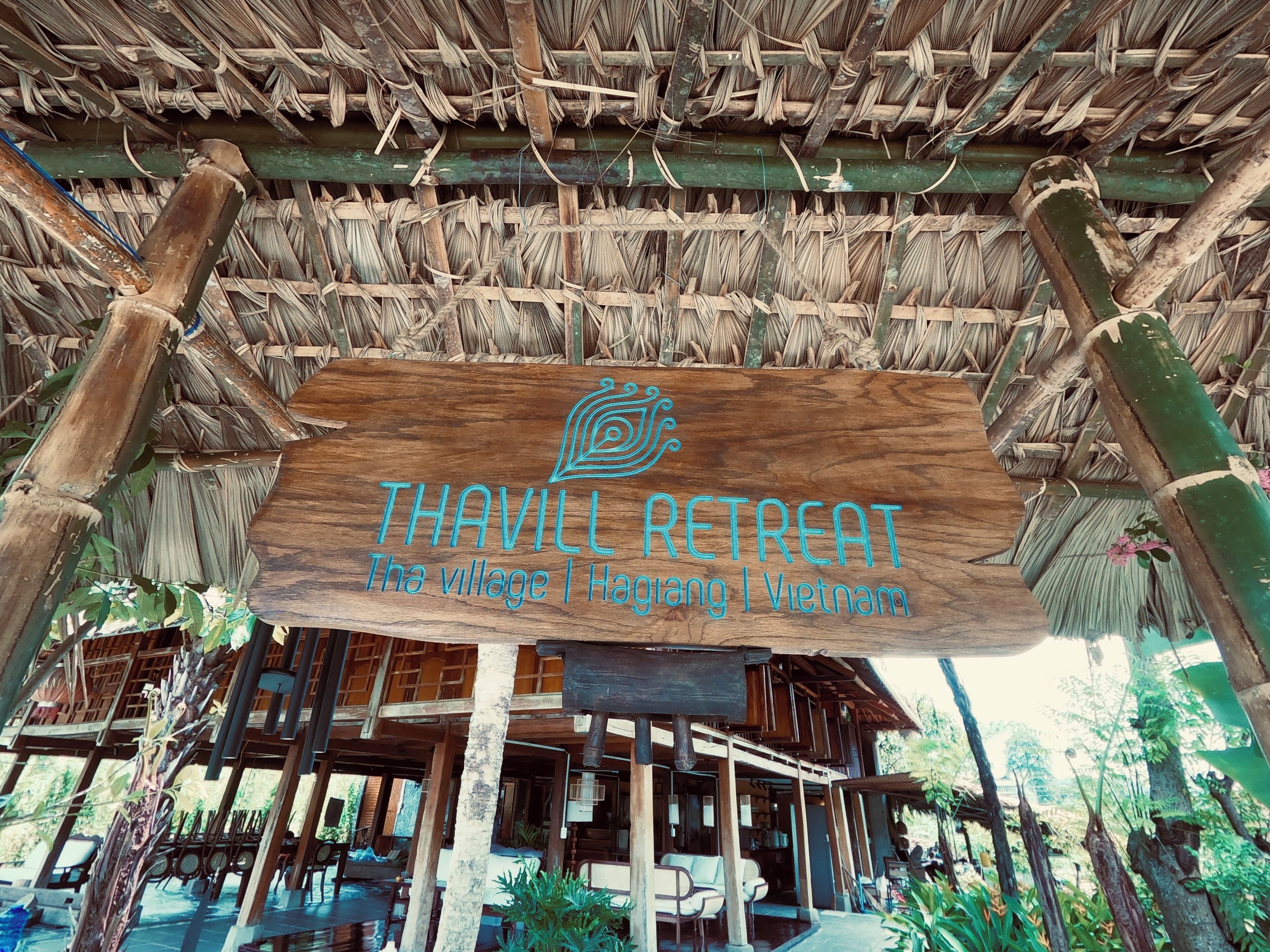 A wooden signboard with the text "THAVILL RETREAT" and "The village | Hanoi | Vietnam" indicating a retreat location.