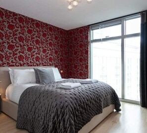 Un dormitorio moderno con una cama grande, un muro estampado y un ventanal amplio.