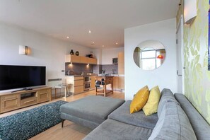 Una sala de estar moderna con una televisión de pantalla plana, un sofá gris y una cocina al fondo.