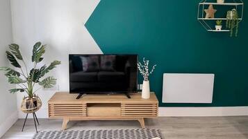 Un salon moderne avec un téléviseur à écran plat posé sur une console en bois, une grande plante en pot et un motif géométrique sur le mur.