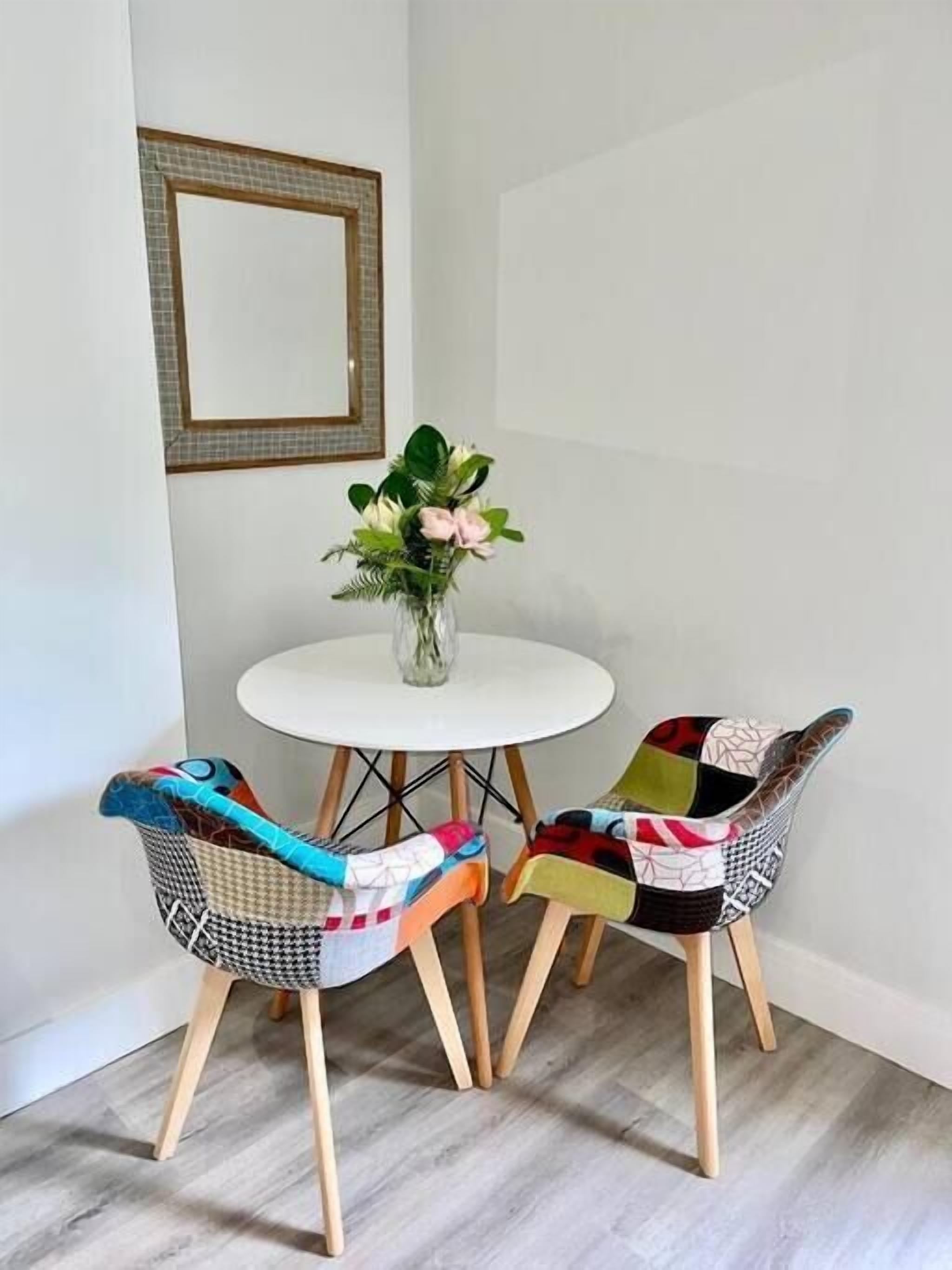 Un petit coin repas avec une table ronde blanche et deux chaises recouvertes d’un tissu coloré.
