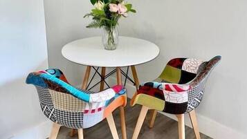 Un petit coin repas avec une table ronde blanche et deux chaises recouvertes d’un tissu coloré.