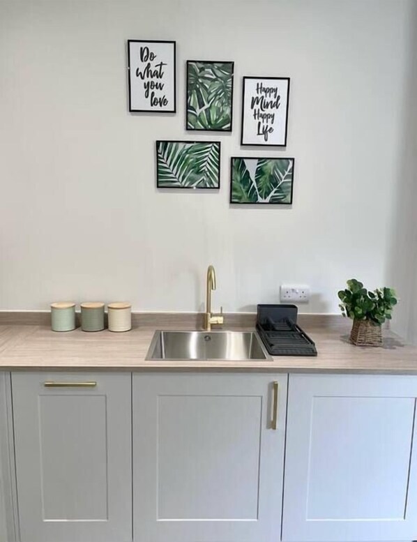 A kitchen with a stainless steel sink, a gold faucet, and three jars on the counter. - Gorgeous New 1-Bed, Town Centre, Parking & Garden (Bournemouth)