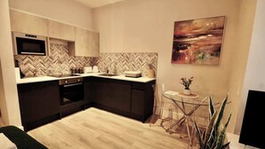 A modern kitchen with a microwave, oven, and herringbone-patterned backsplash. There is a dining area with a glass table and chairs, and a painting on the wall. - Large Studio Apt, Close to Beach w/ Free Parking! (Bournemouth)