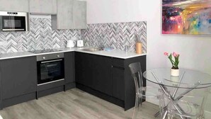 A modern kitchen with a herringbone tile backsplash, a built-in oven, and a glass dining table with chairs. - Large Studio Apt, Close to Beach w/ Free Parking! (Bournemouth)