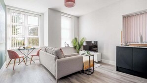 A modern living room with a sofa, TV, and dining area. - Light, Bright & Full of Style. 1-Bed Apt with PKG (Bournemouth)