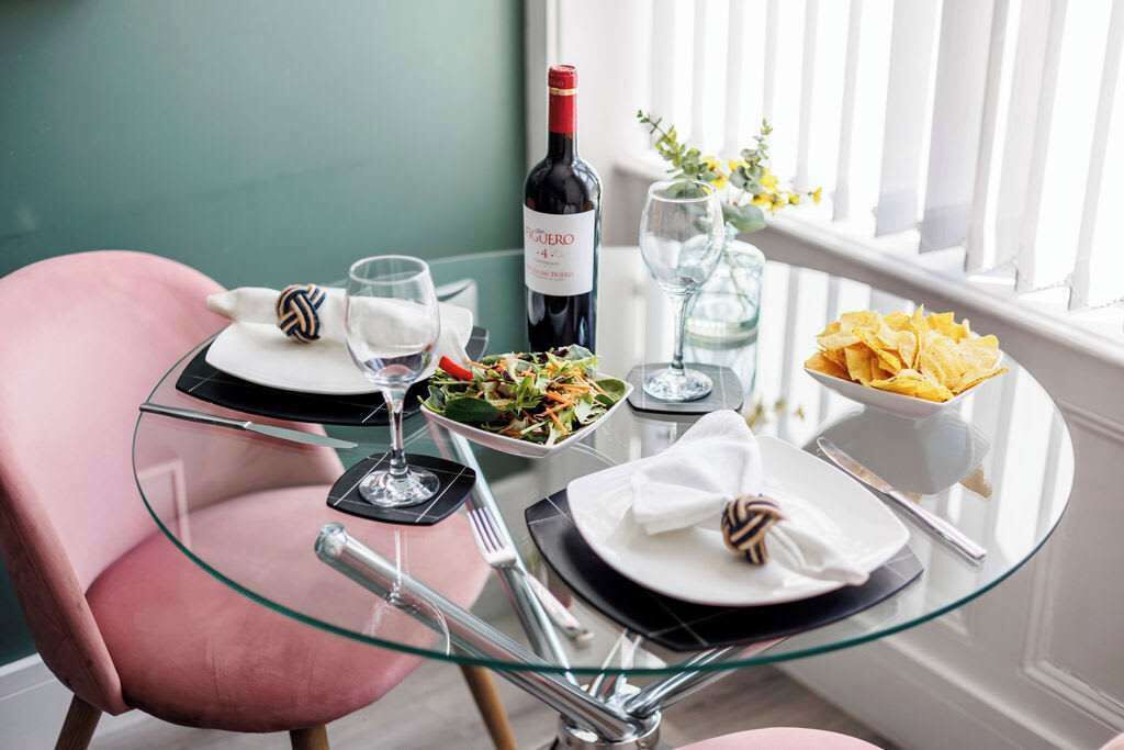 A dining table with a bottle of wine, glasses, plates, and a bowl of chips.
