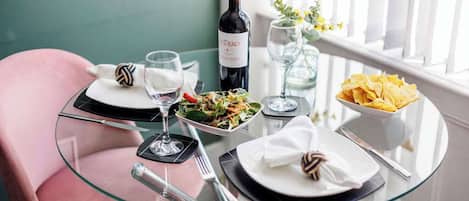 A dining table with a bottle of wine, glasses, plates, and a bowl of chips.
