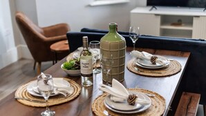A dining table set with plates, glasses, and a bottle of wine, with a large decorative vase and a bowl of salad. - Gorgeous Family 2-Bed Apt w/ Free Gym & Parking (Bournemouth)