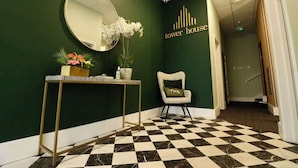 A reception area with a checkered floor, a round mirror, a console table with decorative items, a chair, and a wall sign reading "tower house". - Gorgeous Family 2-Bed Apt w/ Free Gym & Parking (Bournemouth)