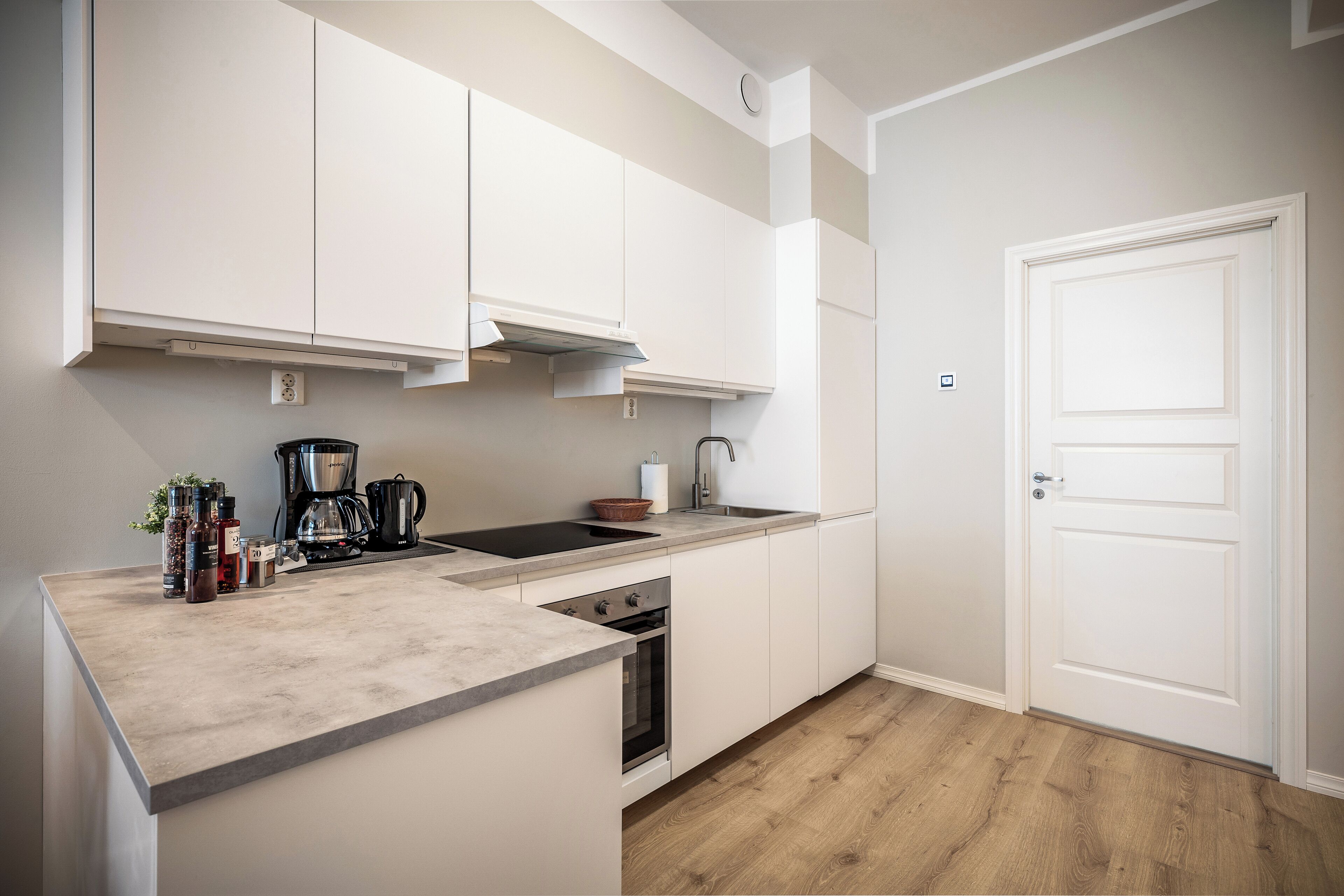 A modern kitchen with white cabinets, a built-in oven, and a coffee maker.