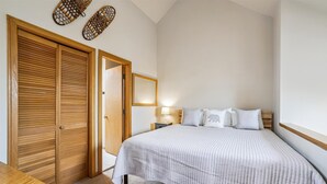 A bedroom with a bed, a wooden wardrobe, a nightstand, and a wall-mounted lamp. - Ski-in 1 bedroom plus loft condo with pool, hot tub, and fireplace. (Killington)